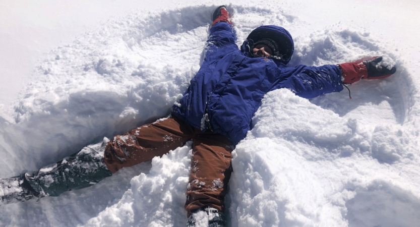 A person wearing winter gear makes a snow angel. 